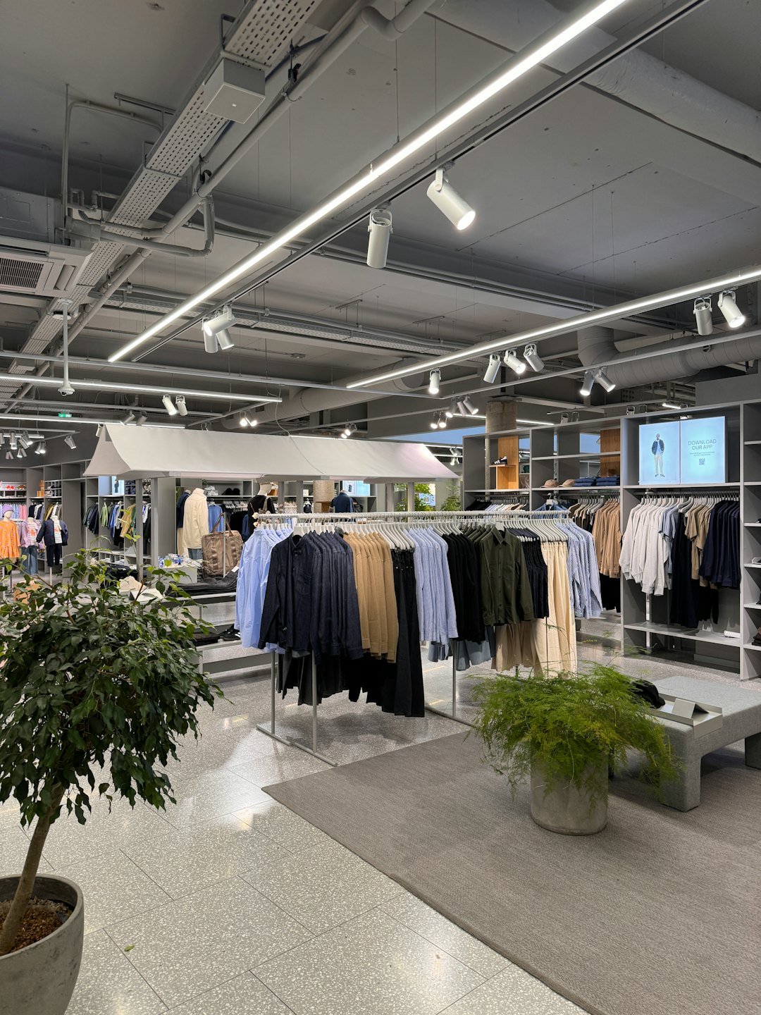 Modern clothing store with racks of clothes and promotional screen.